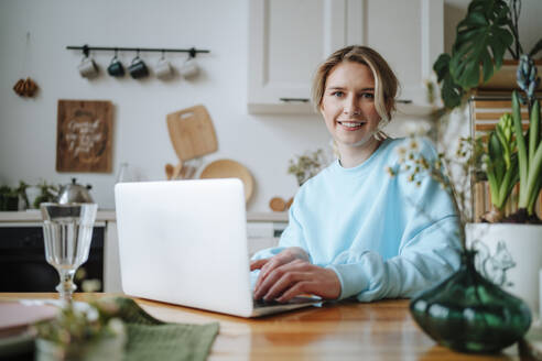Lächelnde junge Frau mit Laptop auf dem Esstisch zu Hause - MDOF01057