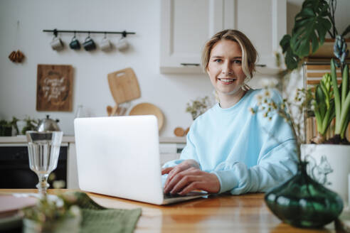 Smiling young woman with laptop on dining table at home - MDOF01057