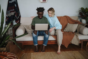 Smiling couple sharing laptop sitting on sofa in living room at home - MDOF01061