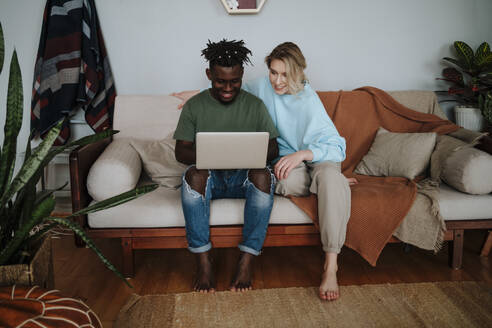 Lächelndes Paar mit gemeinsamem Laptop auf dem Sofa im Wohnzimmer zu Hause - MDOF01061