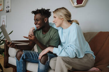 Happy couple sharing laptop sitting on sofa at home - MDOF01065