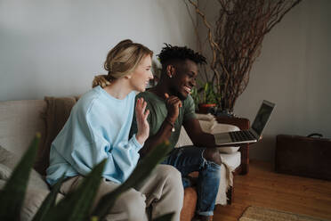 Glückliches Paar gestikuliert bei einem Videogespräch mit Laptop im heimischen Wohnzimmer - MDOF01070