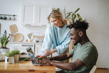 Smiling couple using laptop at kitchen table at home - MDOF01086