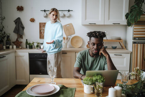 Woman arguing with man sitting with laptop in kitchen at home - MDOF01098