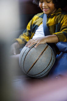 Lächelndes Mädchen sitzt mit Basketball im Auto - IKF00357