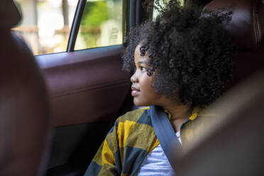 Girl with curly hair looking out of window in car - IKF00359