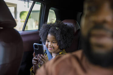 Lächelndes Mädchen, das im Auto sitzend ein Smartphone benutzt - IKF00368