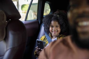 Smiling girl holding smart phone sitting in car - IKF00369