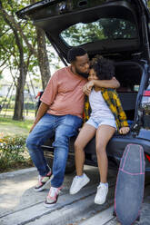 Vater küsst Tochter auf Kofferraum sitzend - IKF00370