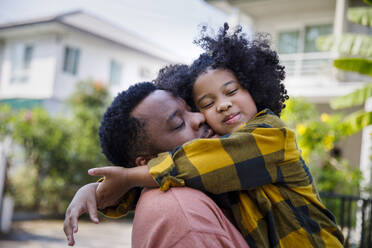 Smiling daughter with curly hair embracing father - IKF00375