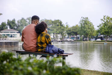 Vater und Tochter schauen auf einer Bank sitzend auf einen Teich - IKF00393