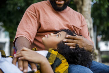 Daughter lying on father's lap at park - IKF00396