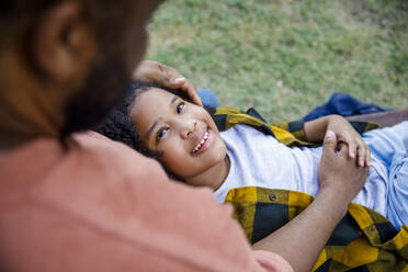 Smiling daughter lying down on father's lap at park - IKF00398