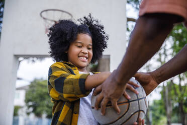 Lächelndes Mädchen nimmt Basketball von Vater am Sportplatz - IKF00403