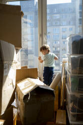 Boy standing amidst cardboard boxes at home - ANAF01303