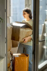 Frau ordnet Pappkartons am Fenster zu Hause - ANAF01310