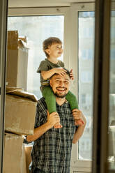 Smiling father carrying boy on shoulders at home - ANAF01316