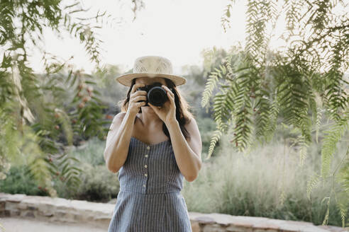 Frau, die durch eine in der Nähe von Pflanzen stehende Kamera fotografiert - LHPF01543
