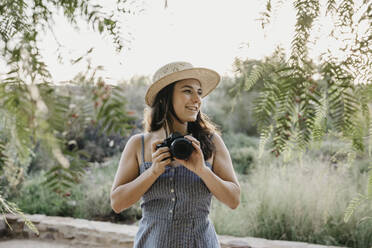 Smiling woman wearing hat holding camera - LHPF01544