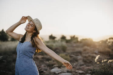 Unbekümmerte Frau mit Hut tanzt auf einem Feld - LHPF01551