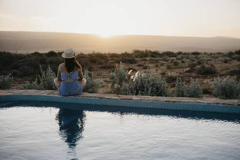 Woman looking at sunset sitting on poolside - LHPF01557