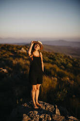Frau mit Hut steht bei Sonnenuntergang auf einem Felsen - LHPF01568