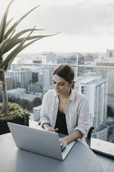 Freelancer using laptop sitting at table on rooftop - LHPF01594
