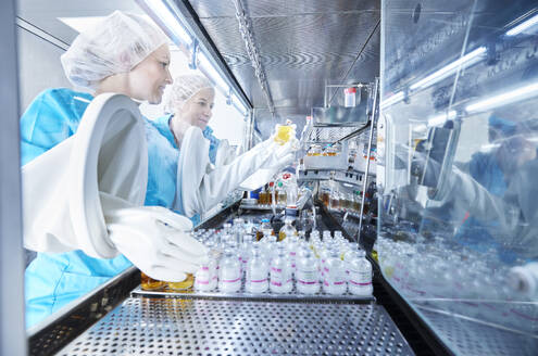 Lab technicians holding chemical bottles inside microbiological safety cabinet - CVF02382