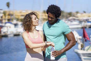 Woman showing smart watch to boyfriend at harbour - JSMF02750