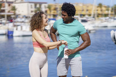 Smiling woman showing smart watch to boyfriend at harbour - JSMF02751