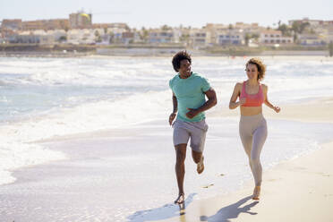 Lächelndes Paar joggt zusammen am Strand - JSMF02759