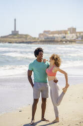 Smiling couple standing face to face with arms around at seashore - JSMF02762