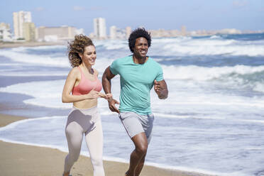 Glückliches Paar in Sportkleidung beim Laufen am Meer - JSMF02763