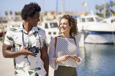 Cheerful couple with camera walking at harbour - JSMF02769