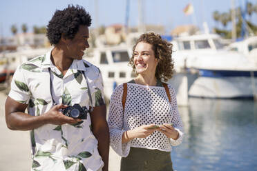 Fröhliches Paar mit Kamera beim Spaziergang am Hafen - JSMF02769