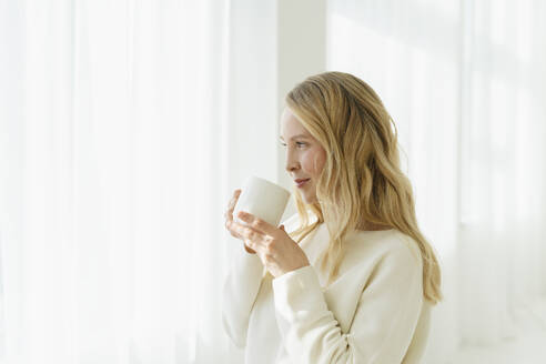 Lächelnde Frau, die vor einem durchsichtigen Vorhang Kaffee trinkt - SEAF01879