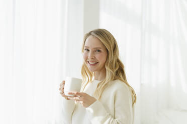 Lächelnde Frau mit Kaffeetasse vor einem durchsichtigen Vorhang - SEAF01880