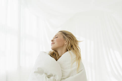 Frau mit geschlossenen Augen, eingewickelt in eine Decke durch einen durchsichtigen Vorhang - SEAF01883