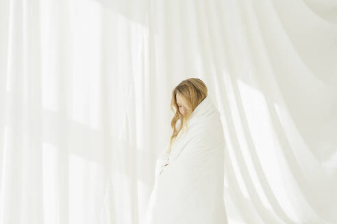 In eine weiße Decke gewickelte Frau vor einem durchsichtigen Vorhang - SEAF01890