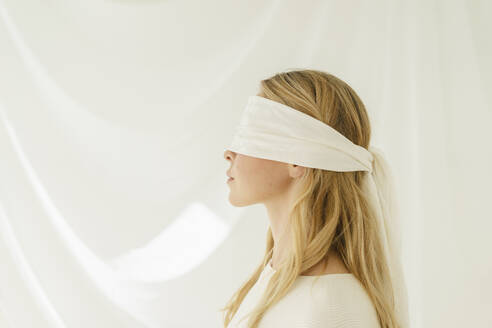 Blonde Frau mit Augenbinde vor durchsichtigem Vorhang - SEAF01910