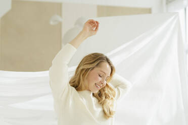 Lächelnde Frau mit erhobenen Armen vor einem Vorhang - SEAF01919