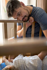 Father putting son to sleep in crib at home - ANAF01324