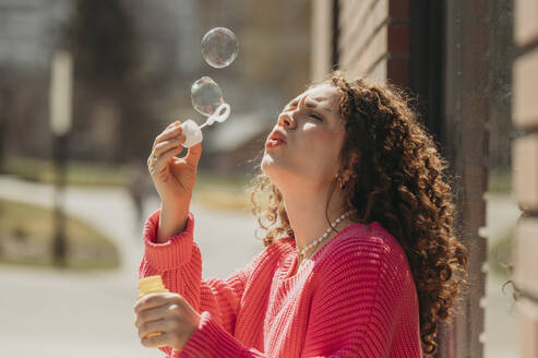 Young woman blowing soap bubbles through wand - ANAF01337