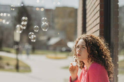 Woman with curly hair blowing soap bubbles - ANAF01338