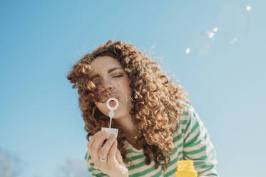 Woman blowing soap bubbles under blue sky - ANAF01339