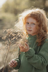 Girl with red hair touching dried plant on sunny day - ANAF01357