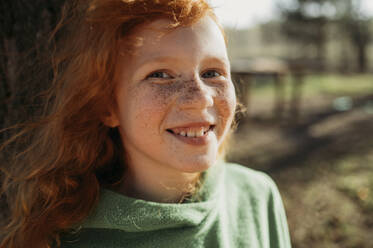 Lächelndes rothaariges Mädchen mit Sommersprossen an einem sonnigen Tag - ANAF01361