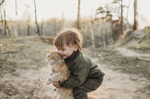 Junge spielt mit Katze im Wald bei Sonnenuntergang - ANAF01373