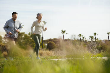 Mature couple running amidst grass at beach - EBSF03240