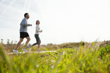 Mature couple running on boardwalk at grassy beach - EBSF03241